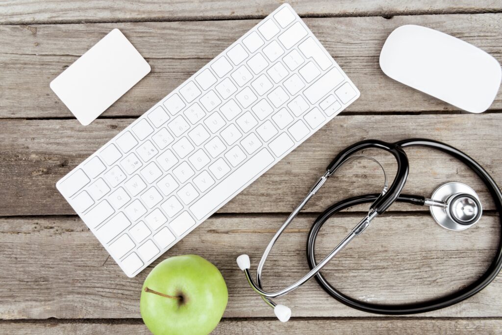 flat lay with digital devices, stethoscope and fresh apple on wooden table