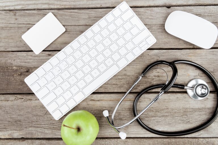 flat lay with digital devices, stethoscope and fresh apple on wooden table